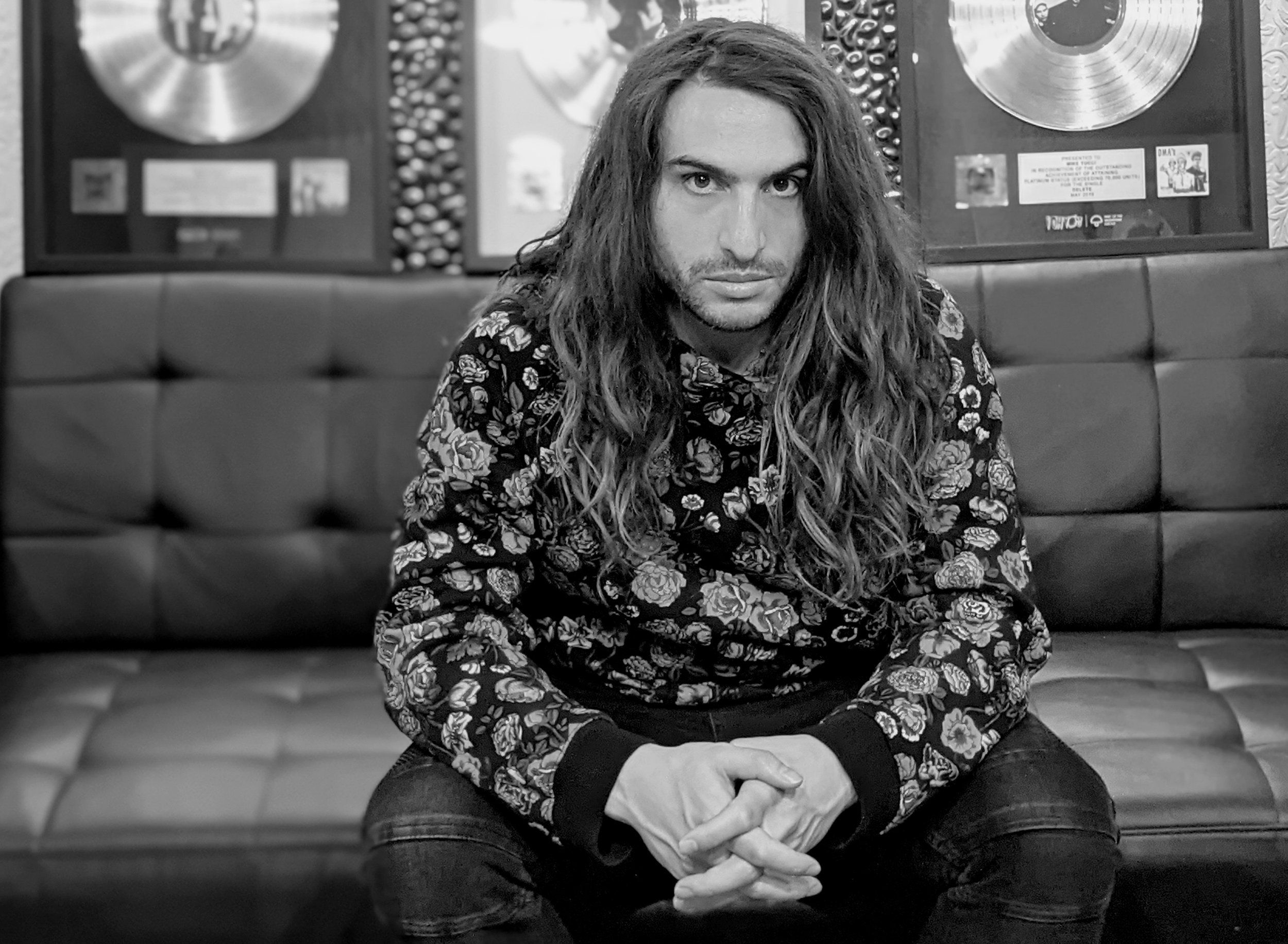 Mike Tucci seated in the mastering studio beneath gold and platinum plaques